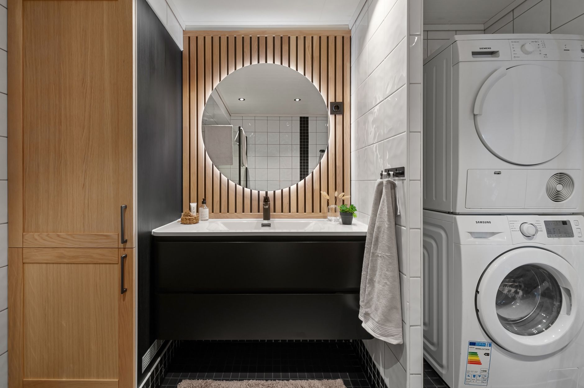 Sleek bathroom featuring a round mirror, modern sink, and integrated washer and dryer.