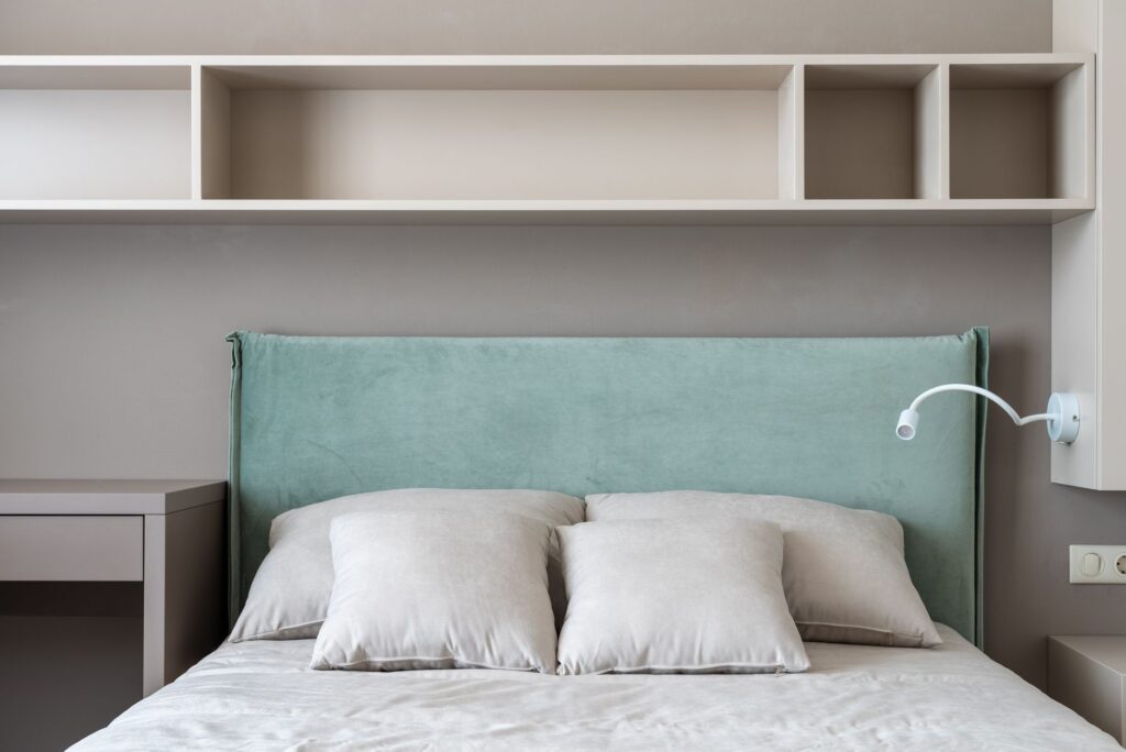 Interior of modern light flat with bed with pillows under shelves near table