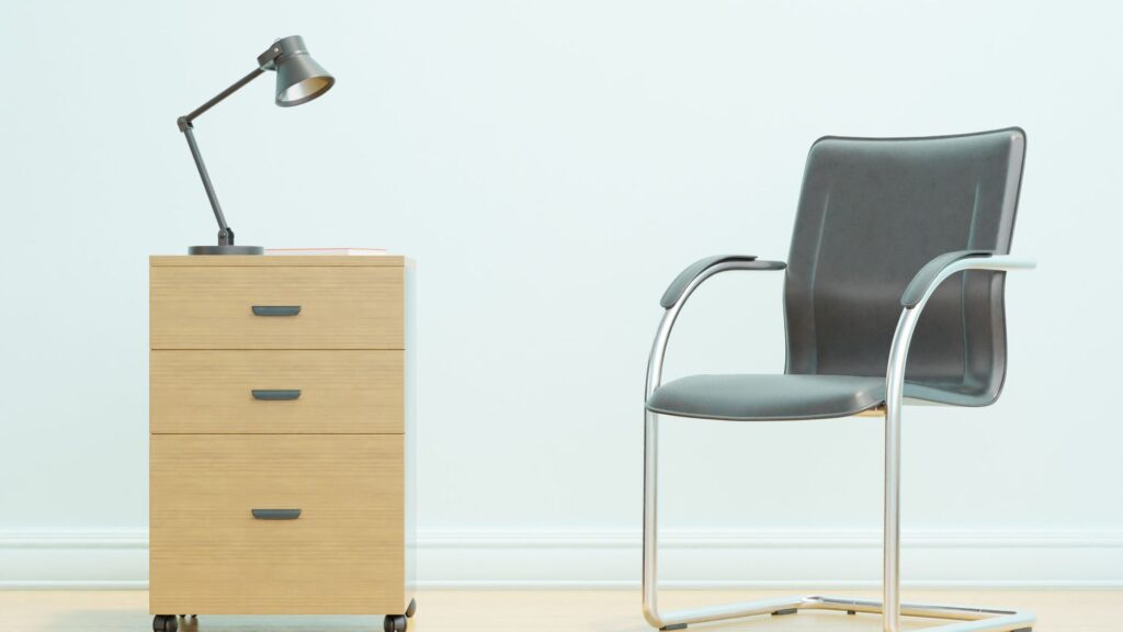 A minimalist office setup showcasing a sleek chair and wooden drawer unit with a desk lamp.