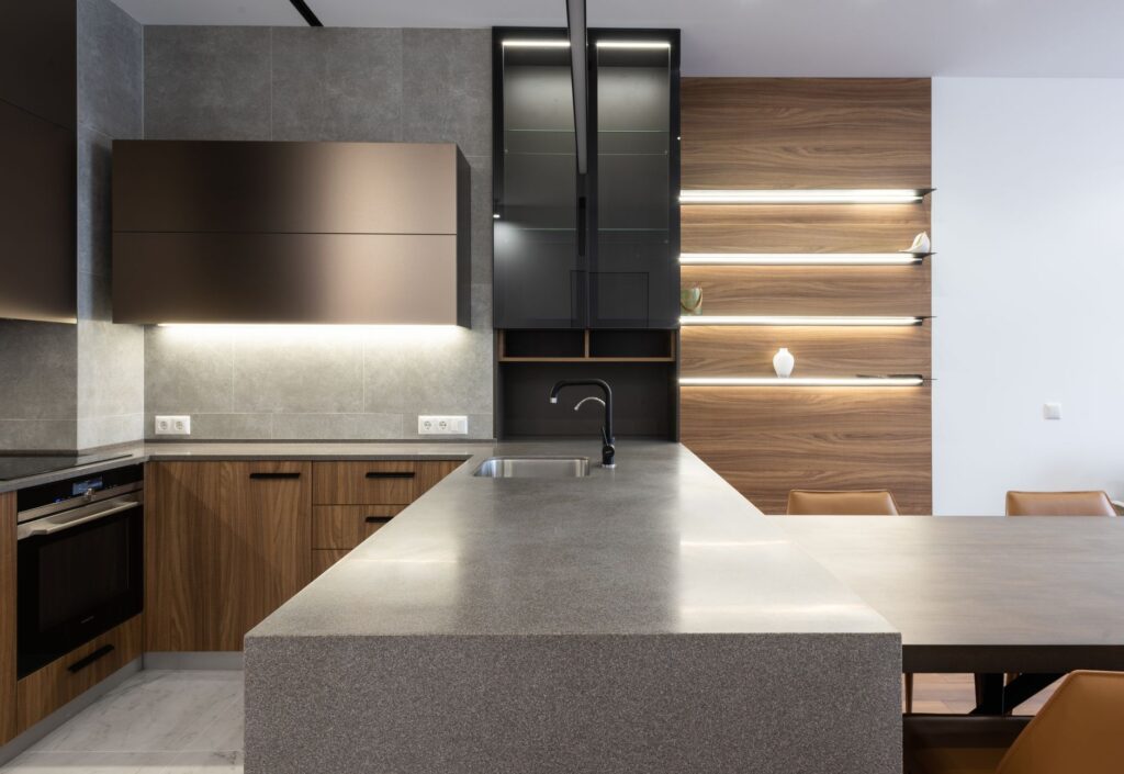 Wooden cupboards with stove placed near gray counter in modern kitchen with light decoration on wall and table in apartment