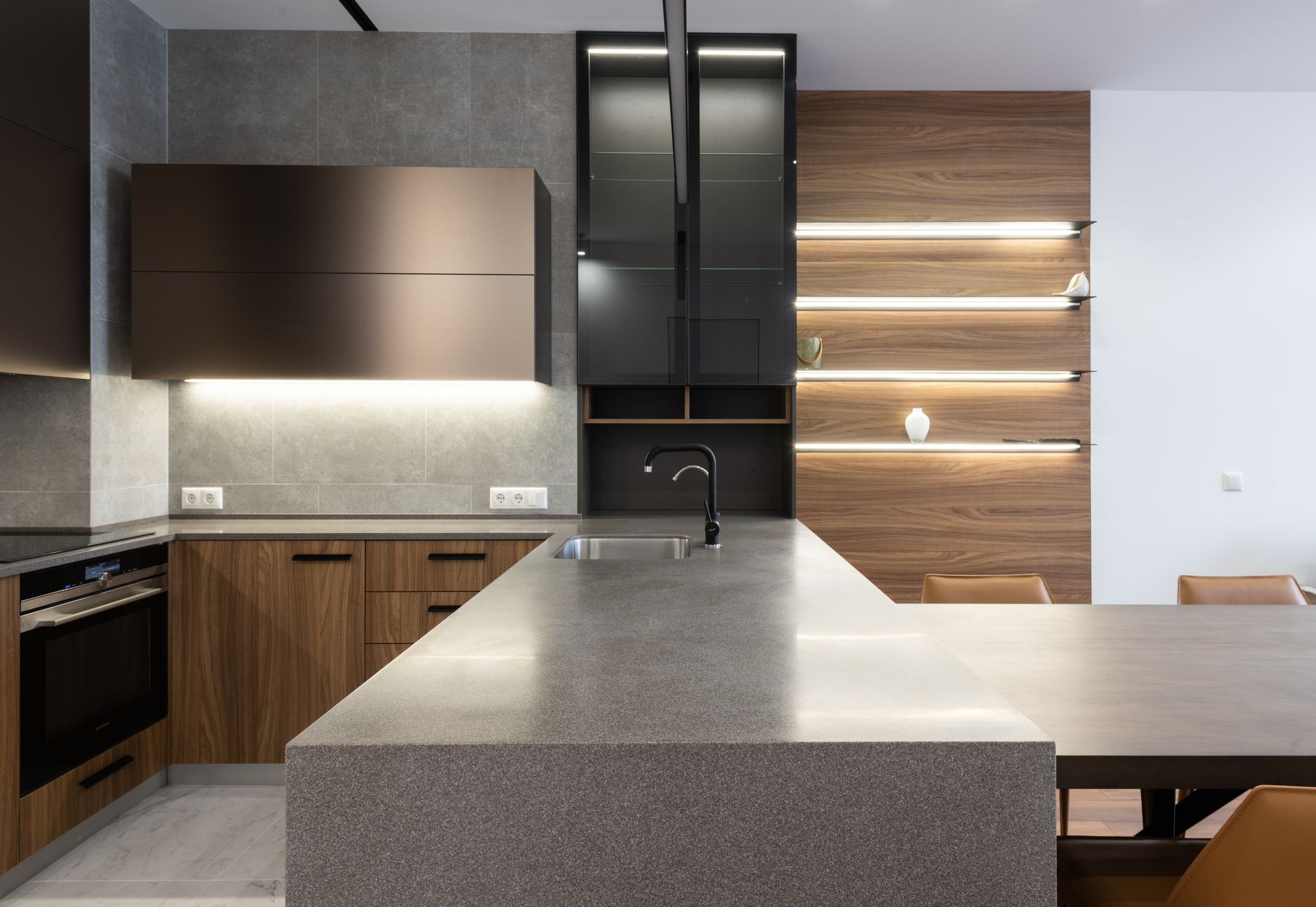 Wooden cupboards with stove placed near gray counter in modern kitchen with light decoration on wall and table in apartment