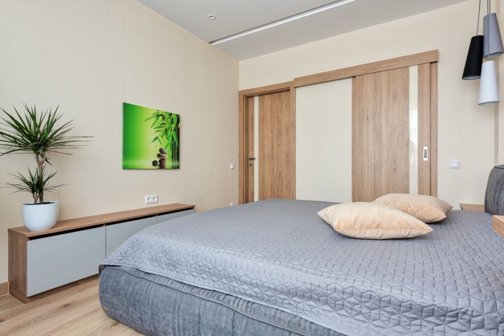 Contemporary bedroom featuring wooden sliding doors, potted plant and cozy bedding.