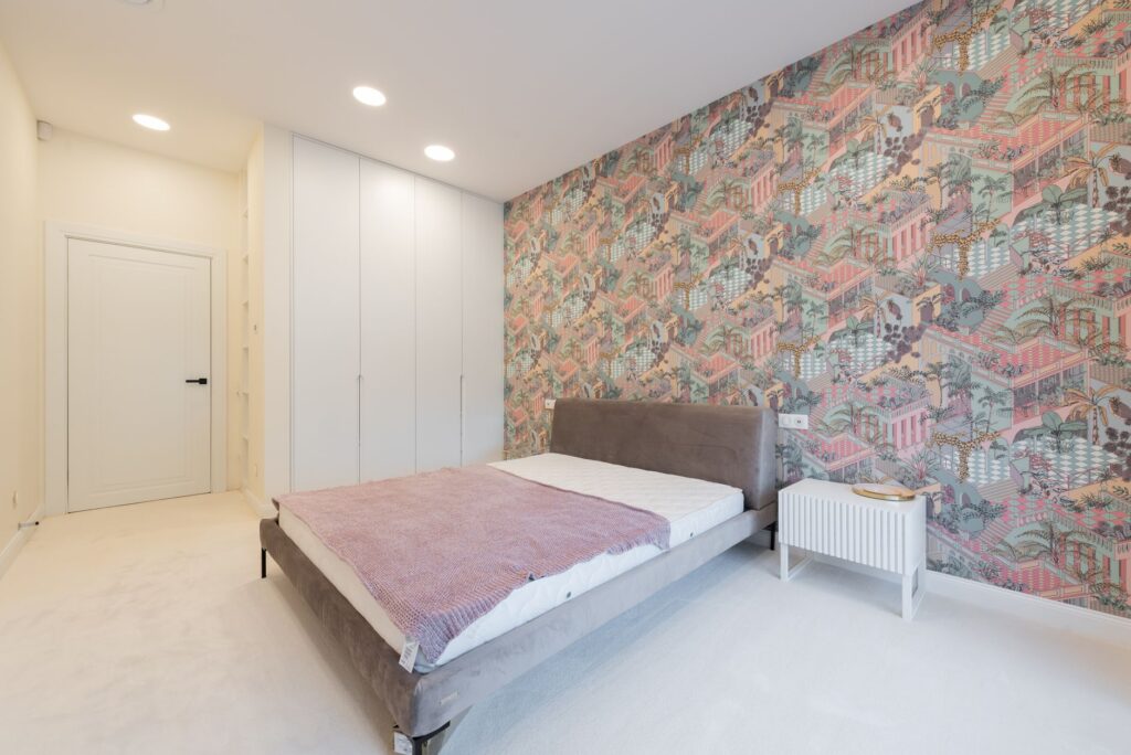 Interior of modern apartment with bed near colorful wall and table near cabinet and door