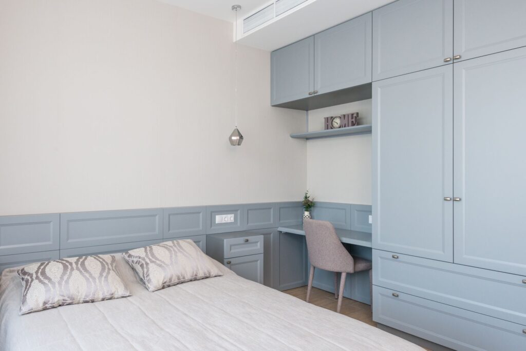 Stylish bedroom features built-in cabinetry, soft blue tones, and a cozy workspace.