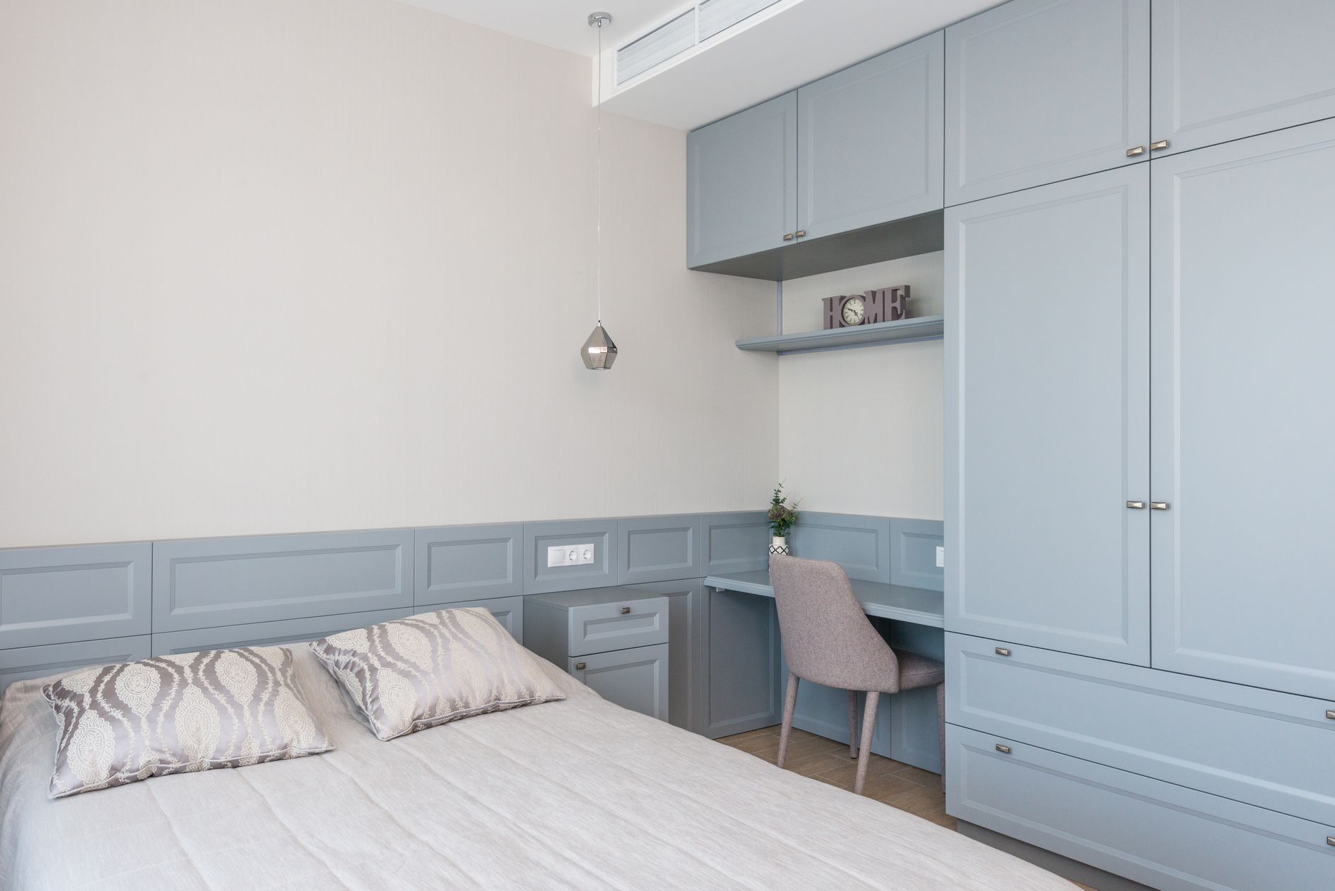 Stylish bedroom features built-in cabinetry, soft blue tones, and a cozy workspace.